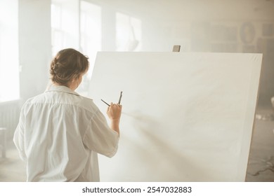 A young female artist working with acrylics on a canvas in a sunlit art studio. - Powered by Shutterstock