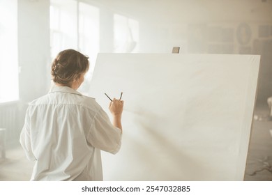 A young female artist working with acrylics on a canvas in a sunlit art studio. - Powered by Shutterstock