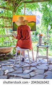 Young female artist working on her art canvas painting outdoors in her garden. Mindfulness, art therapy, creativity and creative hobbies concept.