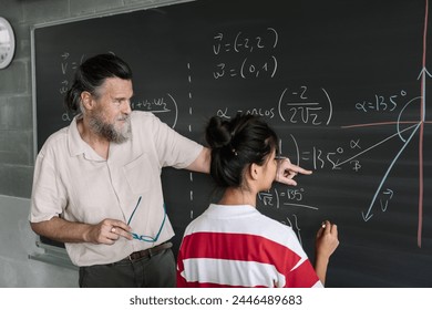 Young Female Asian Teenager Student doing Maths Exercises on Blackboard with help of the teacher in High School - Powered by Shutterstock