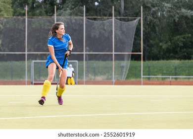 Young female athlete in blue uniform running along the pitch during field hockey game. - Powered by Shutterstock