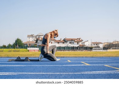 Young female athlete is kneeling on a blue running track, concentrating before a race - Powered by Shutterstock