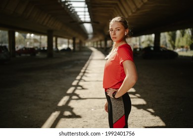 Young Female Athlete Looking At Camera And Holding Hand On Hips. Motivated And Focused Sporty Woman Before A Run.