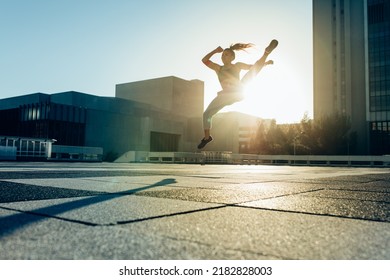 Young Female Athlete Practicing Mid Air Martial Arts Kick In The City. Woman Doing Roundhouse Kick Outdoors.