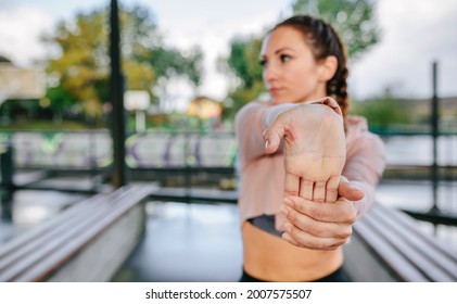 Young Female Athlete Stretching Hands And Wrists Outdoors. Selective Focus On Hand In Foreground