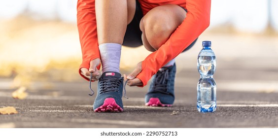 Young female athlete tying shoelaces before running in autumn park, a bottle of water was leading her - Close up.