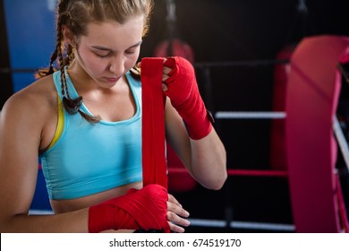 Young female athlete wrapping red bandage on hand in boxing ring at fitness studio - Powered by Shutterstock