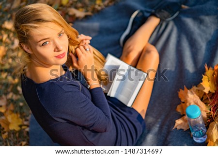 young female in the autumn park. A woman in an autumn park is reading a book, lying on a plaid, autumn reading pleasure.