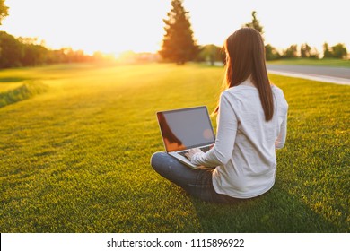 Young female back view. Woman working on laptop pc computer with blank black empty screen to copy space in city park on green grass sunshine lawn outdoors. Mobile Office. Freelance business concept - Powered by Shutterstock