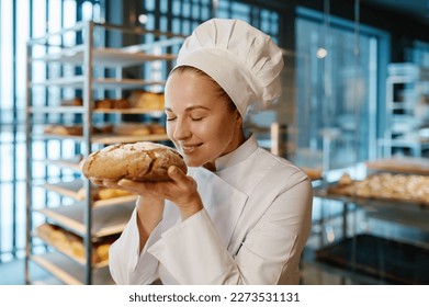 Young female baker smelling fresh bread over modern bakery background - Powered by Shutterstock