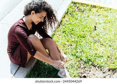 A young female ballet dancer laces up her pointe shoes on a sunny day outside - Powered by Shutterstock