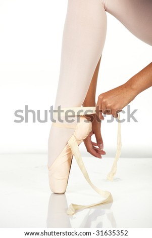 Young female ballet dancer showing how to tie a ballet Pointe Shoe against a white background. NOT ISOLATED