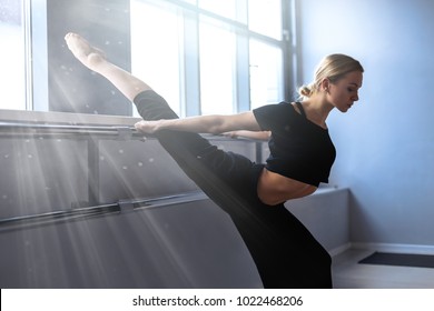 Young female ballet dancer is stretching in the studio with white walls