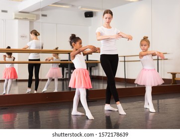 Young female ballet teacher and two little girls in classical dance school