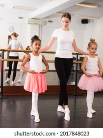 Young female ballet teacher and two little girls in classical dance school