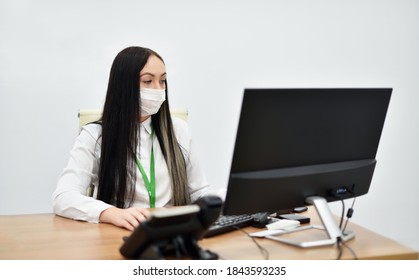 A Young Female Bank Employee In A Face Mask Works With A Desktop Computer In The Office