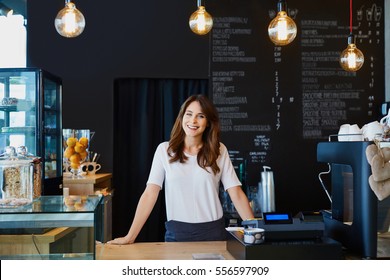 Young female barista standing behind the bar in cafe smiling
