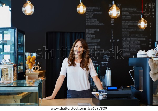 Young female barista standing behind the bar in\
cafe smiling