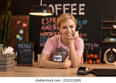 Young Female Barista With Tip Jar At Table In Cafe