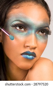 Young Female Beauty Fashion Model Of Mixed Creole And African-American Ethnicity Covered In Dramatic Blue Make-up And Holding Makeup Brush