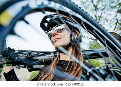 Young female biker carries a mountain bike on her back