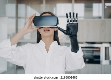 Young female with bionic prosthetic arm wearing virtual reality glasses. Modern women with disability touches objects in VR, raised artificial robotic hand. Medical high technologies concept.