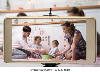 Young Female Blogger Online Influencer Mom With Grandmother And Two Daughters, Live Streaming A Parent Playing With Children Show On Social Media Using A Smartphone.