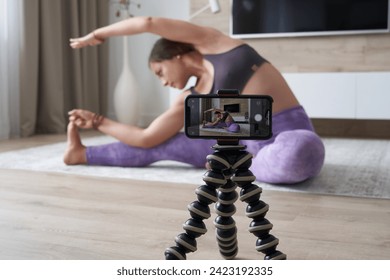 Young female blogger recording sports video at home doing yoga in living room - Powered by Shutterstock