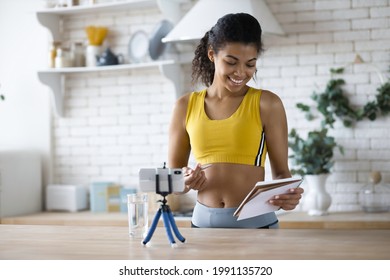 Young Female Blogger Shoot Social Media Vlog On Smartphone, Handsome African American Woman Fitness Vlogger Record Streaming Video About Fitness And A Healthy Lifestyle At Home In The Kitchen