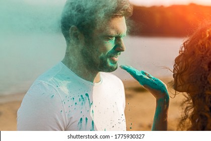 Young female blowing blue powder on face of male while having fun during paint festival on beach - Powered by Shutterstock