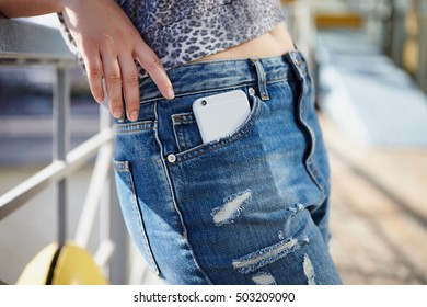 Young Female In Blue Jeans With Huge Modern Silver Mobile Phone In Pocket. Close Up, Focus On Gadget.Buy New Mobile Phone.Popular Gadget Model