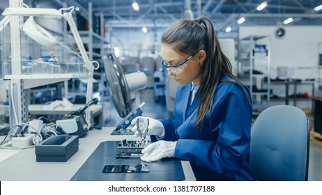 Young Female Blue and White Work Coat is Using Plier to Assemble Printed Circuit Board for Smartphone. Electronics Factory Workers in a High Tech Factory Facility. - Shutterstock ID 1381707188