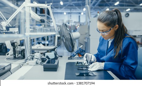 Young Female Blue and White Work Coat is Using Plier to Assemble Printed Circuit Board for Smartphone. Electronics Factory Workers in a High Tech Factory Facility. - Shutterstock ID 1381707194