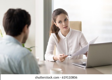 Young female boss talking to employee, pointing to a document, businesswoman discussing papers with partner, hr manager holding job interview asking male candidate about working experience  - Powered by Shutterstock