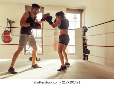 Young female boxer practicing punching combinations with her personal trainer. Sporty young woman having a training session in a boxing gym. - Powered by Shutterstock