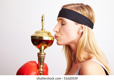 Young female boxer with red boxing gloves kissing a trophy - Powered by Shutterstock