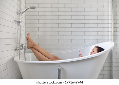 Young female browsing internet on mobile phone while taking bath and relaxing in bathtub - Powered by Shutterstock