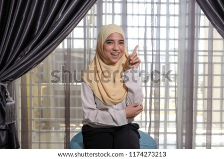 A young female businesswoman wearing hijab smiling happily while showing idea hand gesture
