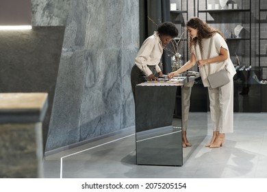 Young female buyer and shop assistant bending over display with jewelry while pretty consumer choosing bracelet - Powered by Shutterstock