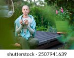 Young female cancer patient sitting on garden patio with coffee, eyes closed. Health insurance, medical expenses, loss of income safety plan. Mental health, wellbeing, meditation during illness.