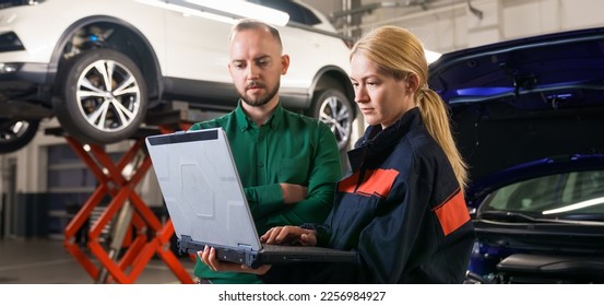 A young female car mechanic holds a diagnostic laptop and shows the manager the identified errors against the background of the car. Panoramic photography - Powered by Shutterstock