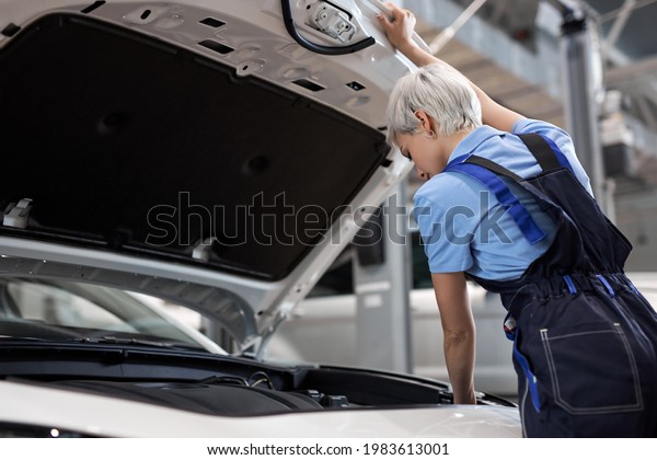 Young female car\
repair worker. Caucasian woman mechanic check the oil level in car\
engine. Mechanic checking and maintenance car engine or vehicle\
with herrself. Side view