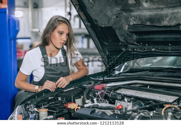 Young female from car\
service in a black jumpsuit and white t-shirt standing near the\
broken car. The girl opened the hood and looked at the engine.\
Refit woman car 