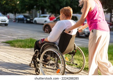 Mujer joven cuidadora empujando silla de ruedas con una persona con discapacidad en la calle de la ciudad