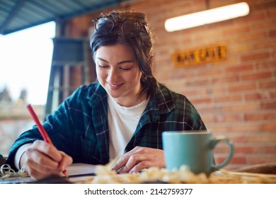 Young Female Carpenter Drawing And Measuring Woodwork Design In Garage Workshop