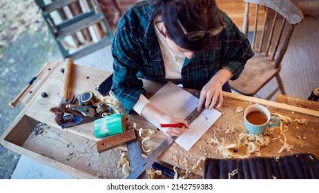 Young Female Carpenter Drawing And Measuring Woodwork Design In Garage Workshop