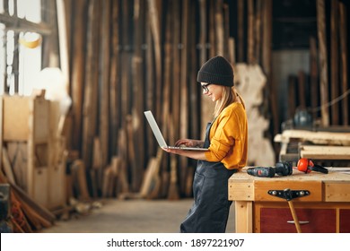 young female carpenter looks drawings on a laptop during  while  break in working with wood in modern handicraft studio