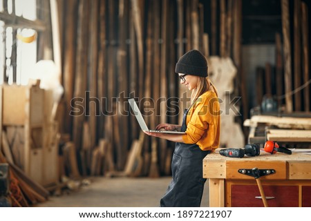 young female carpenter looks drawings on a laptop during  while  break in working with wood in modern handicraft studio Foto d'archivio © 