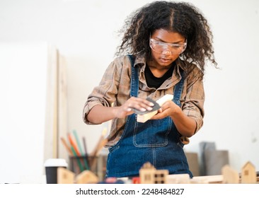 Young female carpenter is working in woodwork DIY furniture in carpentry workshop. Multiracial woman woodworker using sandpaper to rub lumber plank at a workbench. Skill craftsman and DIY woodworking. - Powered by Shutterstock