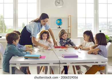 Young Female Caucasian Teacher Working With Little Children Group In Classroom Explaining. Woman Tutor And Schoolkids Joining Puzzle. Preschool Or Primary School Education And Development